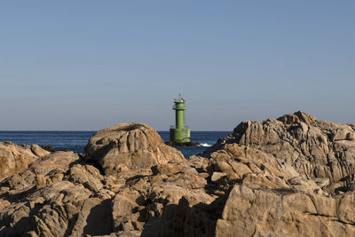 Lighthouse amidst rocks and sea against sky