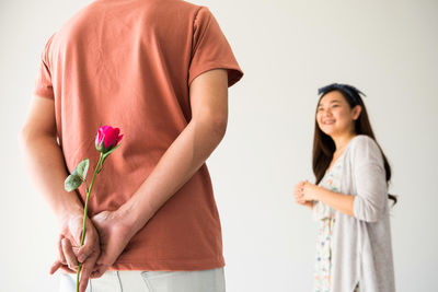 Young woman holding rose while standing against white wall