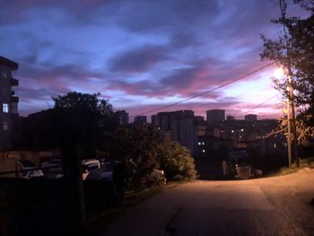 Street amidst buildings against sky at sunset