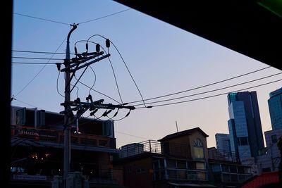 Low angle view of electricity pylon and buildings against clear sky