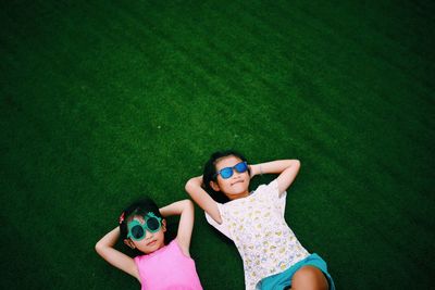 High angle view of friends wearing sunglasses lying on grassy field at park