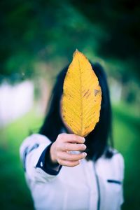 Close-up of woman covering face with yellow leaf outdoors