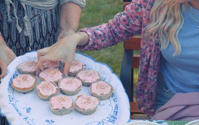 Midsection of women holding cupcakes in yard