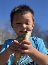 Cute boy holding fish against sky