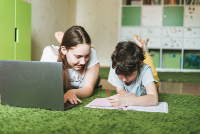 Siblings girl teenager and tween boy do homework writing in pupil book with opened laptop 
