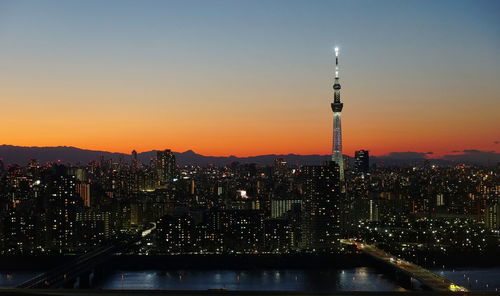 Illuminated cityscape with tower against sky at dusk