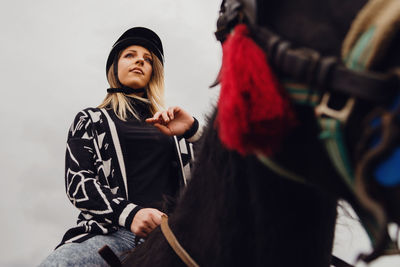 Woman looking away while sitting on horse against sky