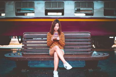 Full length portrait of woman sitting on bench