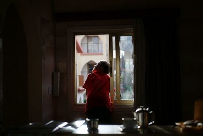 Rear view of boy looking up through window at home