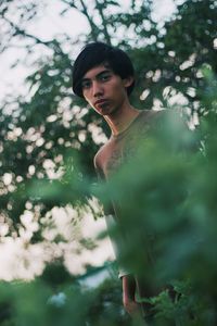 Portrait of young man standing against tree