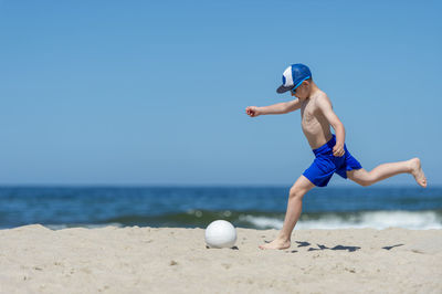 Full length of shirtless man at beach against blue sky