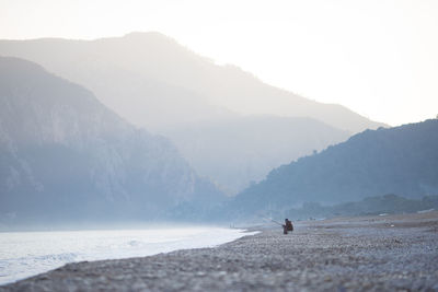 Side view of man fishing at sea shore against clear sky