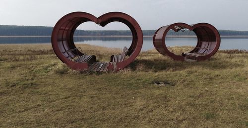 Metallic structure on field by lake against sky