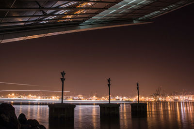 Illuminated factory by river against sky at night