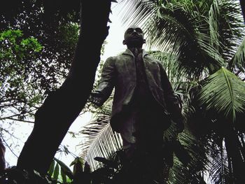 Low angle view of statue by palm tree against sky