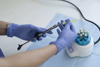 Hands of anonymous dentist in latex gloves putting vial with anesthesia into syringe over table in clinic