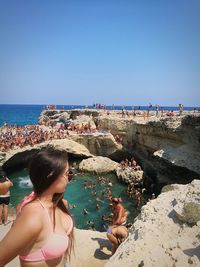 Woman in bikini standing at beach against clear sky