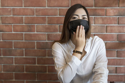 Portrait of woman standing against brick wall