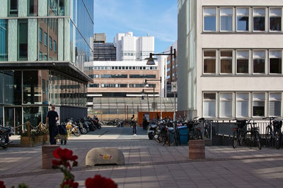 People on street by modern buildings in city against sky