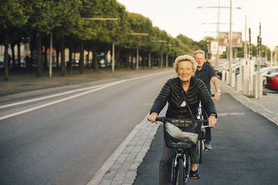 Portrait of smiling senior woman with man riding bicycles on city street