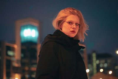 Portrait of young woman standing against illuminated light at night