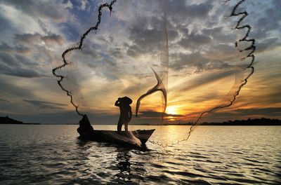 Fisherman throwing net in sea during sunset