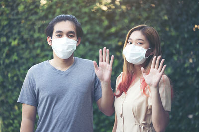 Young asia couple in protective masks showing stop gesture at garden home person