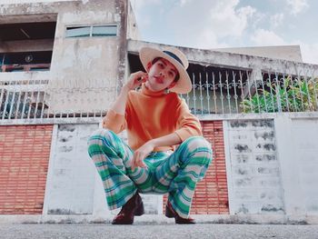 Full length of smiling man sitting against brick wall