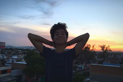 Boy standing by tree against sky during sunset