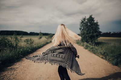 Young blond woman on dirt road against sky