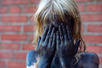 Girl covered in powder paint while hiding face against brick wall