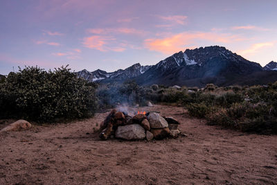 Campfire flames in stone firepit in desert at base of mountain at sunset