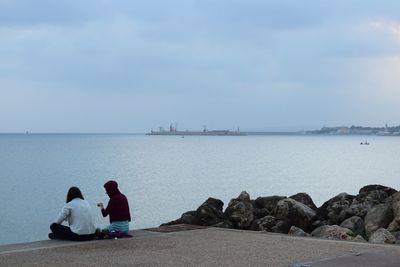 Rear view of people sitting on sea against sky