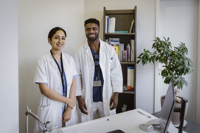 Portrait of confident male and female healthcare workers standing by desk at clinic