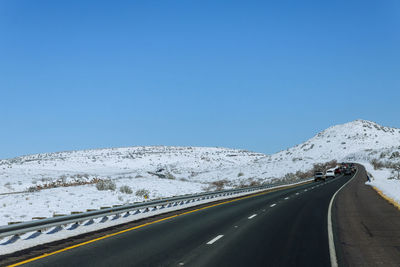 Road leading towards snowcapped mountains against clear blue sky