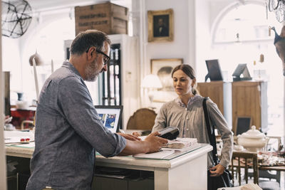 Owner using card reader in front of female customer at shop counter