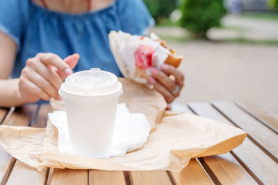 Closeup of woman eating fast food in street cafe, mockup white coffee cup, focus on foreground