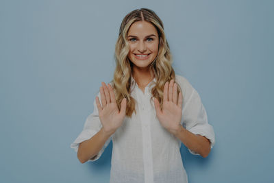 Portrait of young woman standing against blue background