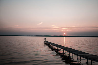 Silhouette person standing on pier over sea against sky during sunset