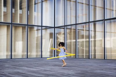 Full length of girl playing with ribbon against modern building