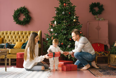 Beautiful stylish young family sitting on the floor near the christmas tree. family members exchange