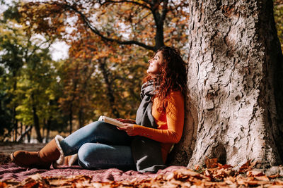 Young woman looking away while sitting on tree trunk