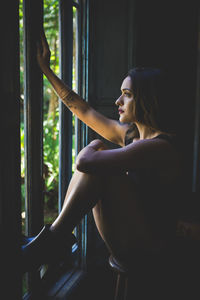 Side view of woman looking away while sitting on window