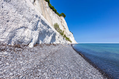 Rock formations by sea against clear blue sky