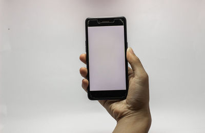 Close-up of hand holding smart phone against white background