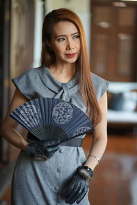 Close-up of woman holding folding fan indoors