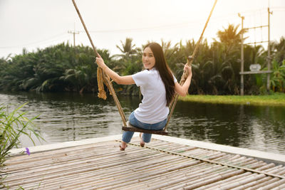 Full length of woman sitting on swing over lake against sky