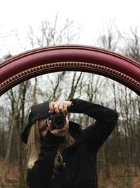 Woman snapping a photo in a red framed mirror with cold forest reflecting 