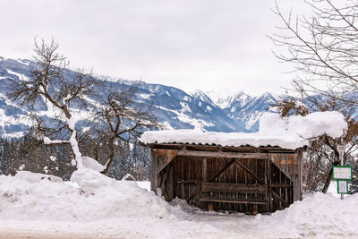 Old, wooden ski bus stop. snow covered mountains and field against sky. austria