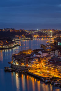 Illuminated buildings by river against sky at night